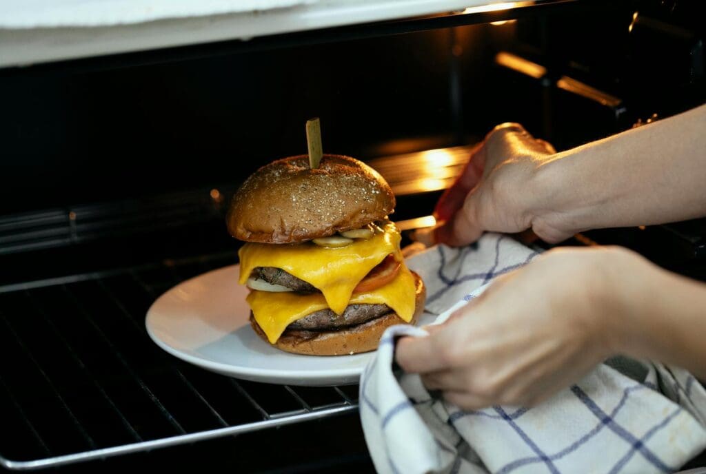 From above of unrecognizable person using towel to place burger served on plate in hot oven on rack while cooking