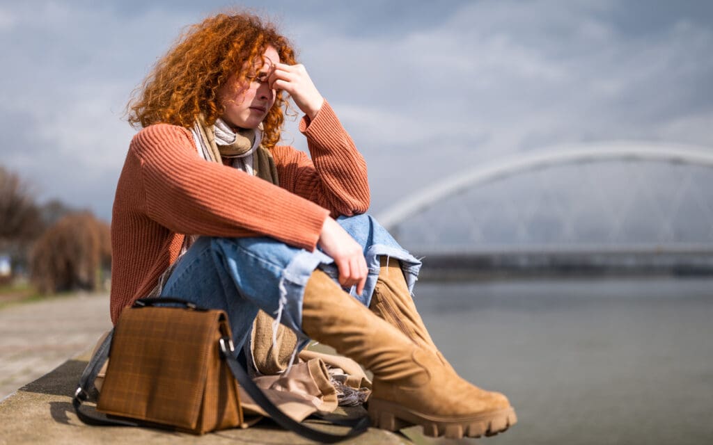 stressed woman sitting on the ground next to a river
