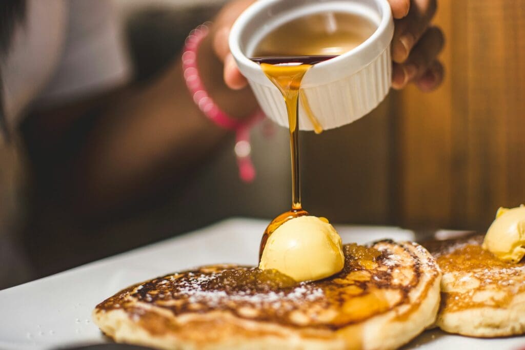person pouring maple syrup into pancake