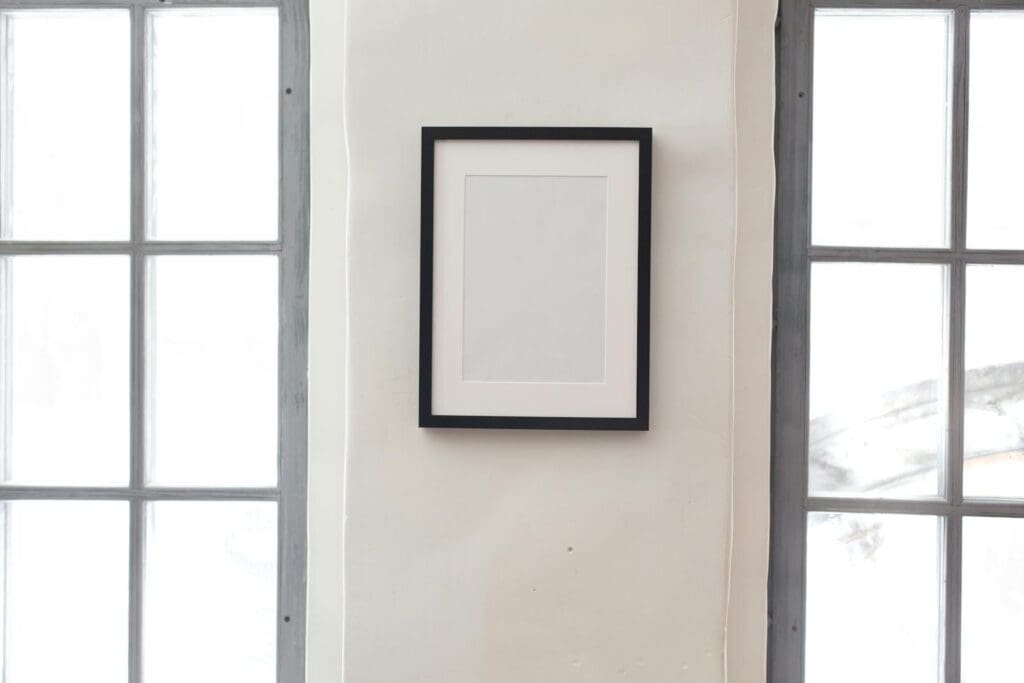 Interior of simple apartment with blank frame on white wall between rectangular shaped windows