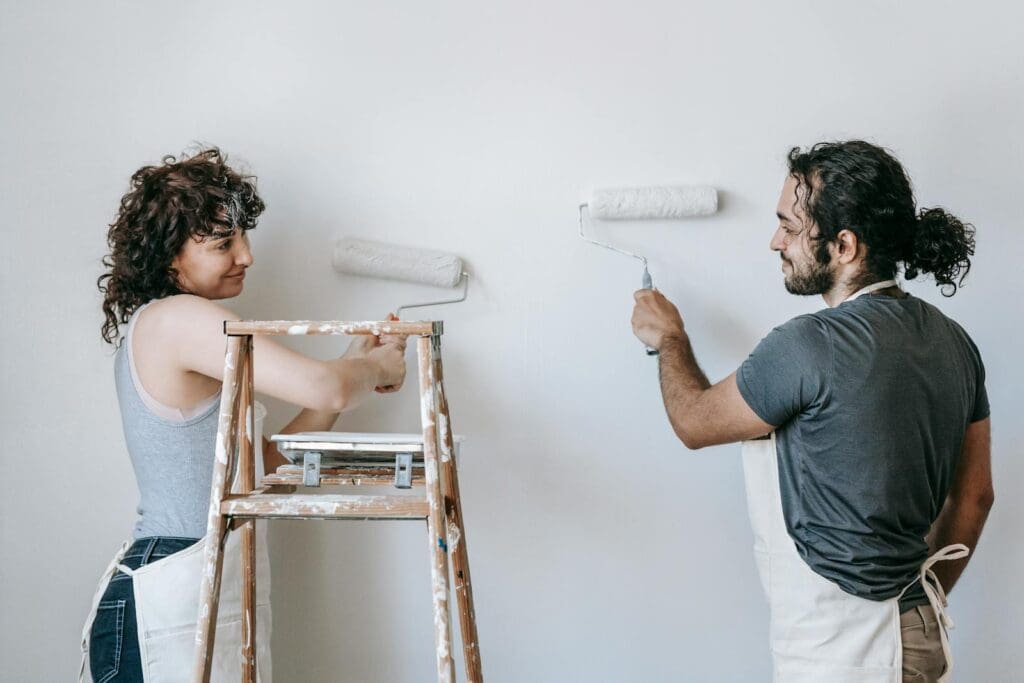 Smiling ethnic couple painting wall with roller brushes at home
