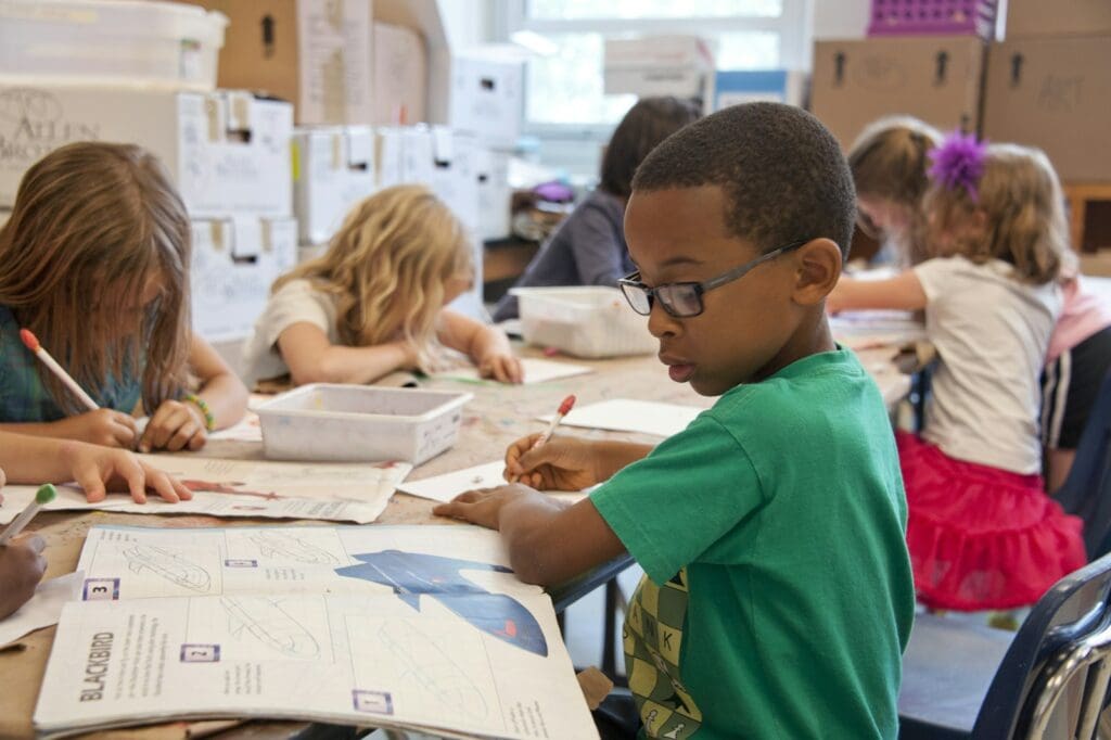 boy in green sweater writing on white paper