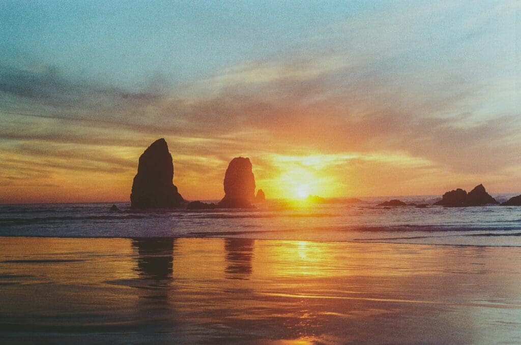 the sun is setting over the ocean with rocks in the water