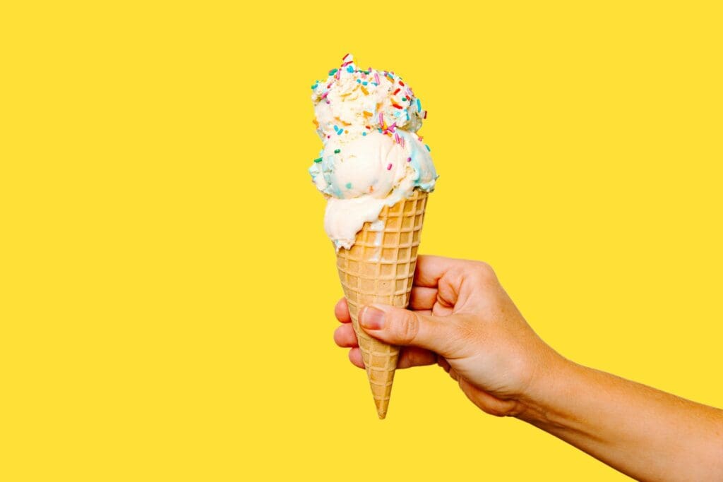 A hand holding an ice cream cone with sprinkles