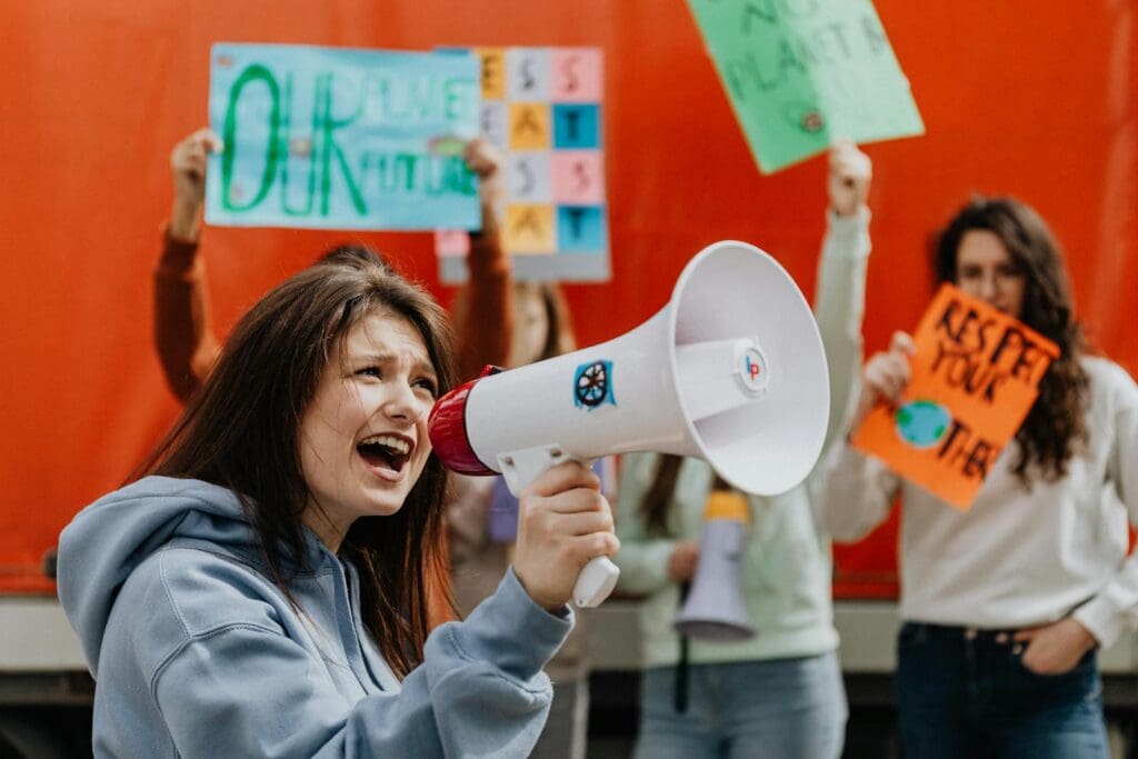 A Woman Talking on the Megaphone Near Protesters Holding Placards