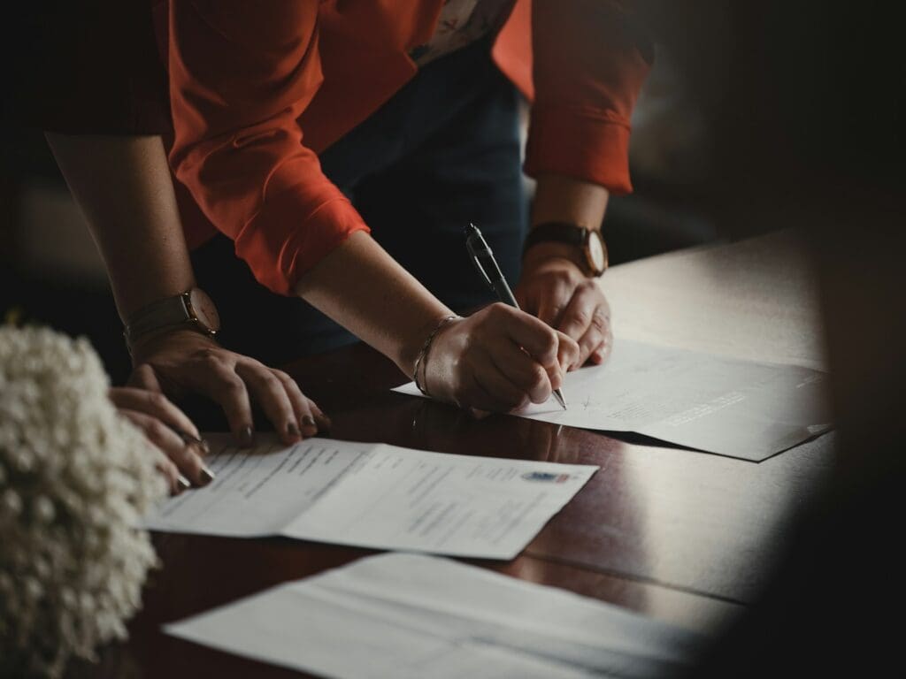 person in orange long sleeve shirt writing signature on white paper