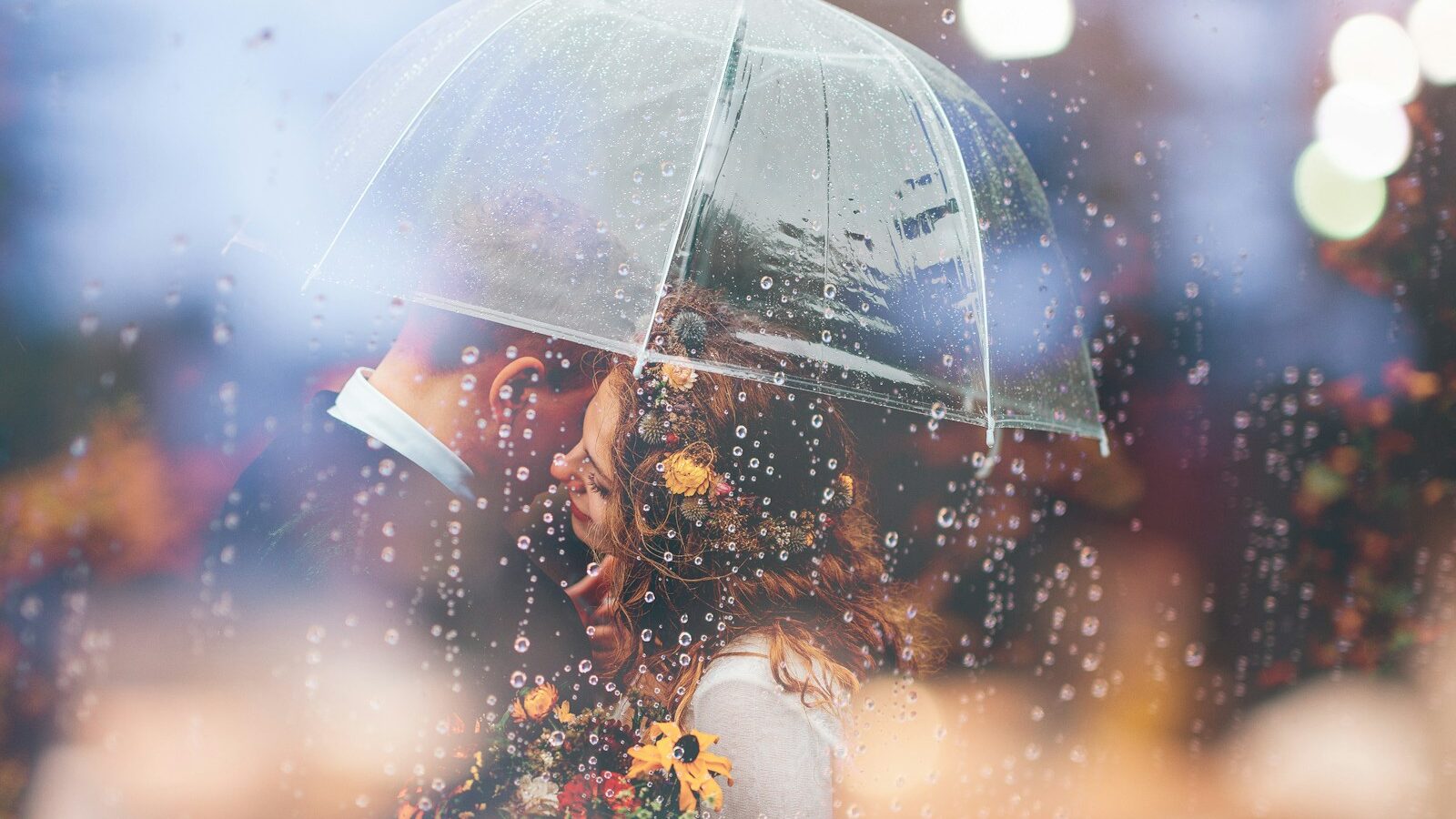 a bride and groom kiss in the rain under an umbrella