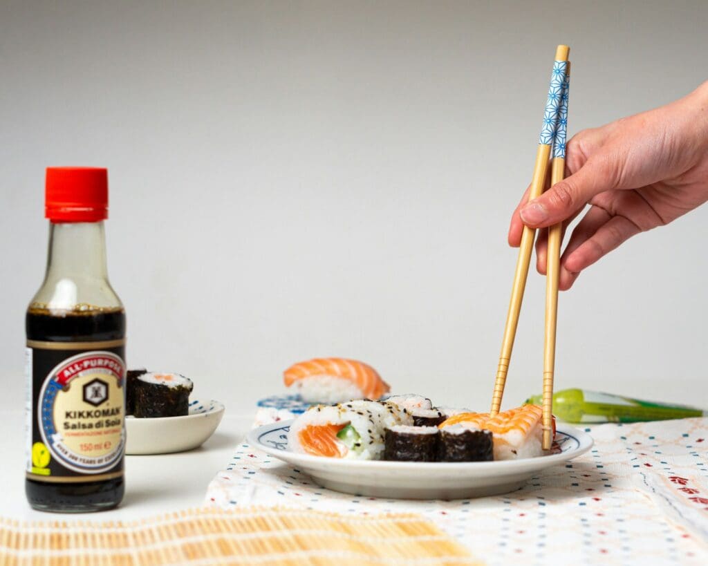 a person holding chopsticks over a plate of sushi