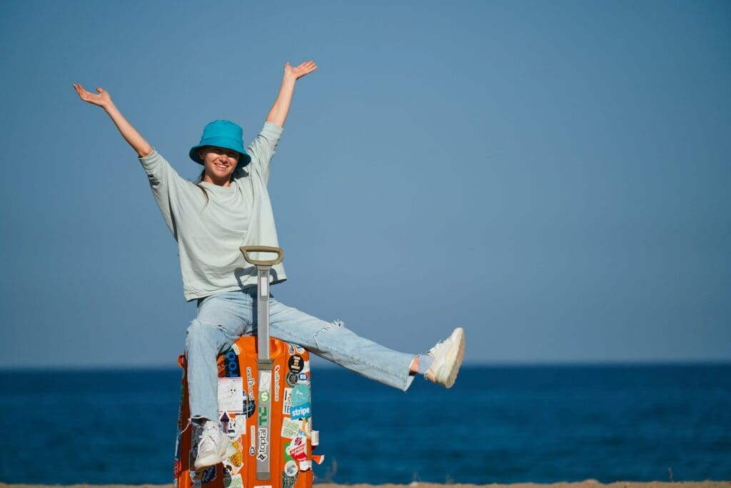 a woman sitting on top of a suitcase on the beach