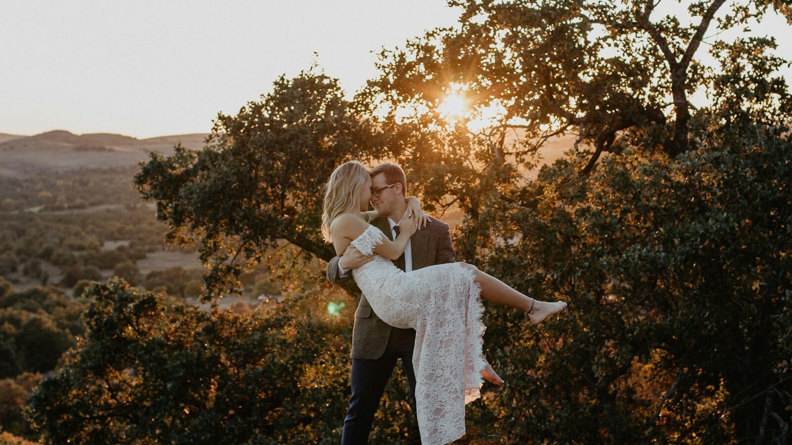 man carrying woman wearing white dress during sunrise