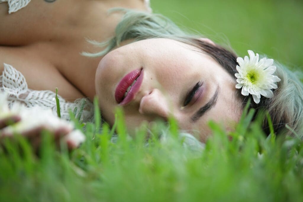 a woman laying in the grass with a flower in her hair