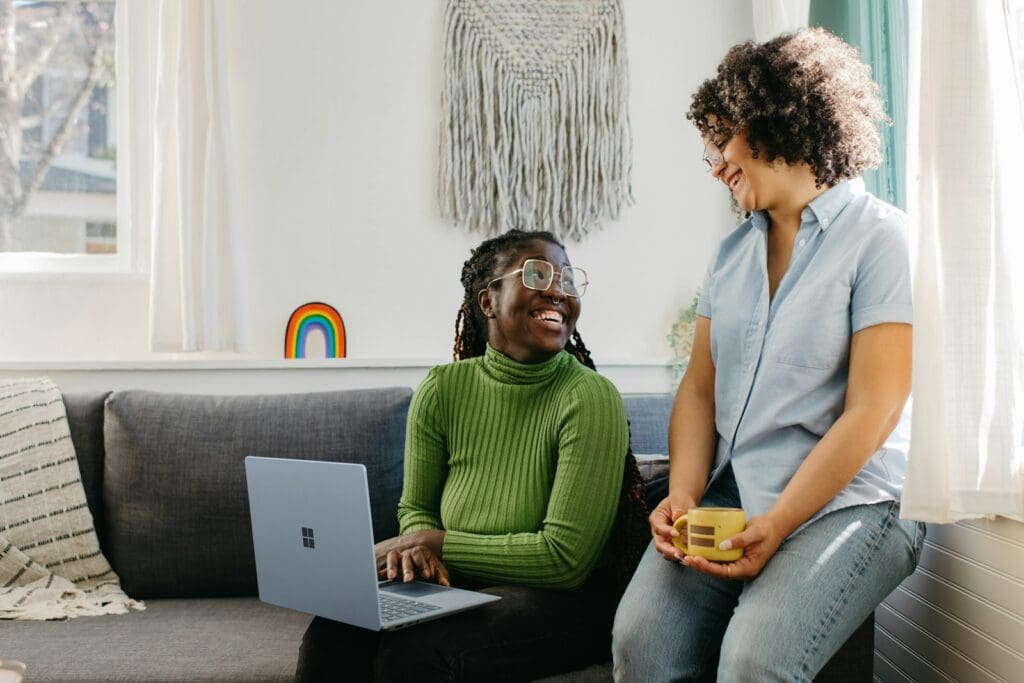 a woman sitting on a couch next to a woman on a laptop