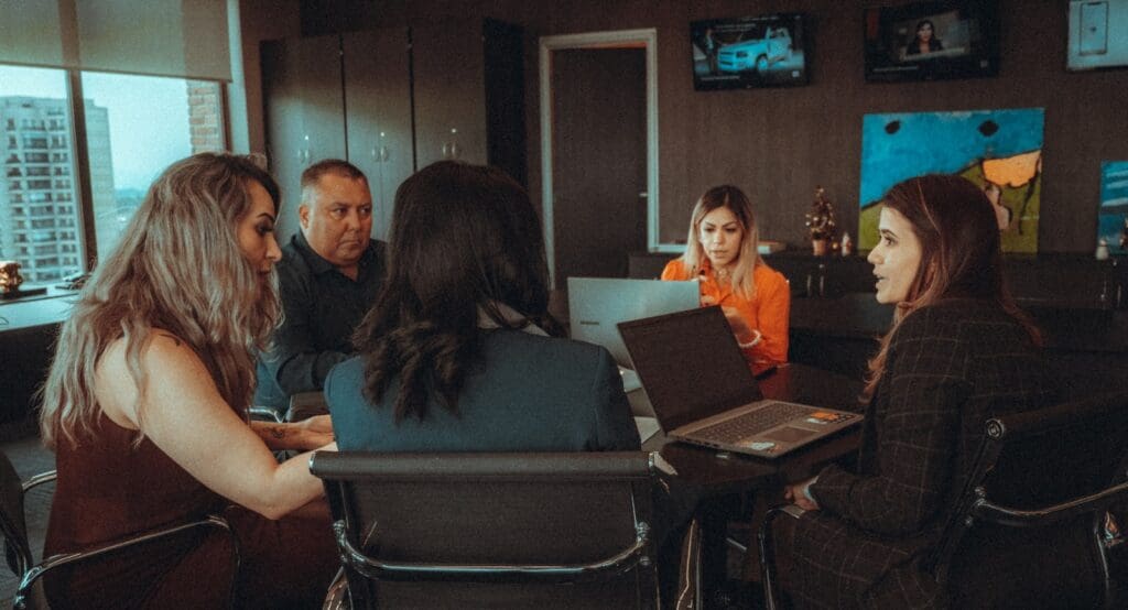 a group of people sitting around a table with laptops