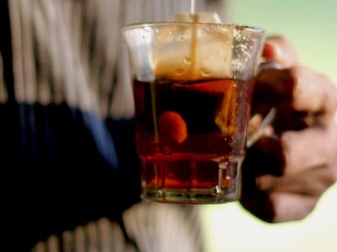 person holding clear shot glass with brown liquid