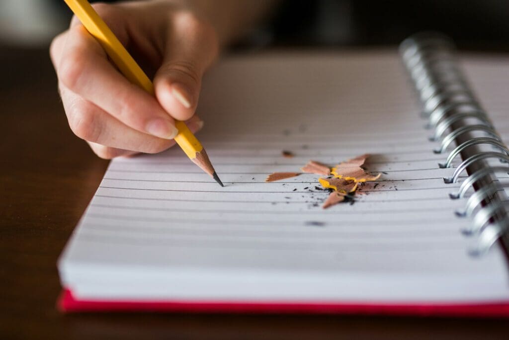 person holding pencil writing on notebook