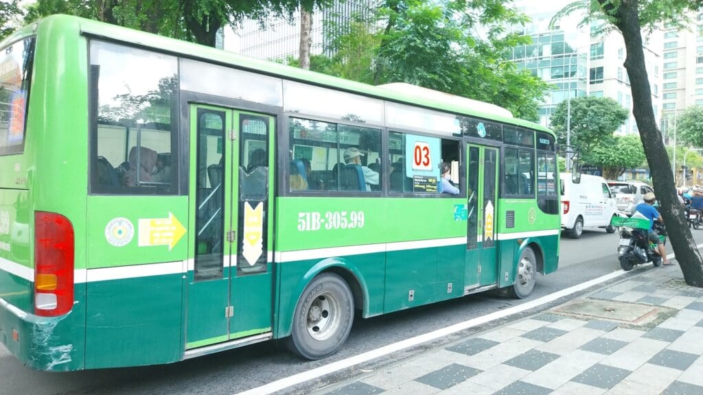 a green bus driving down a street next to tall buildings