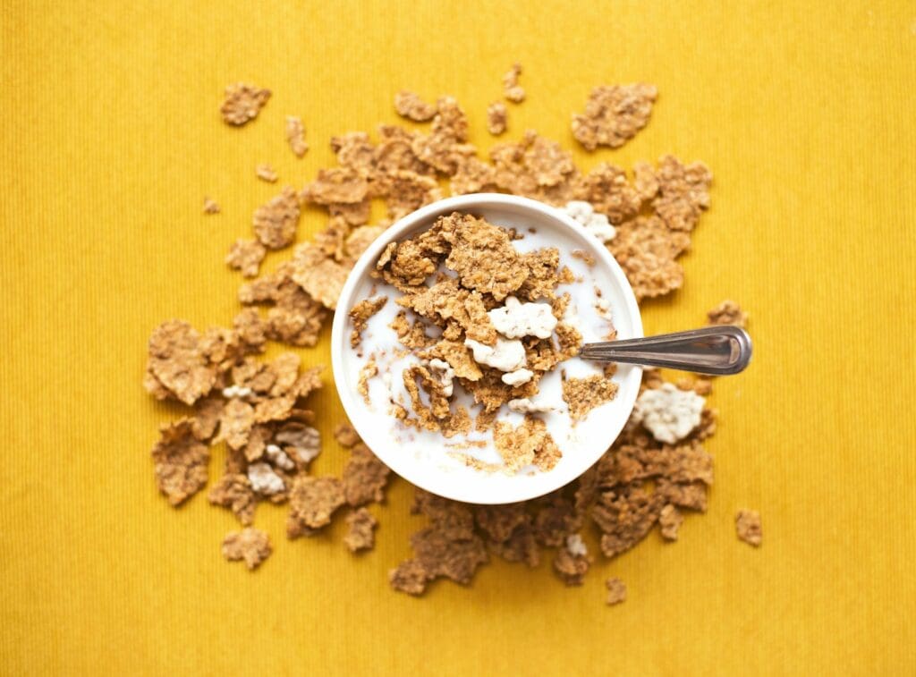 top view of corn flakes in bowl with milk and silver spoon