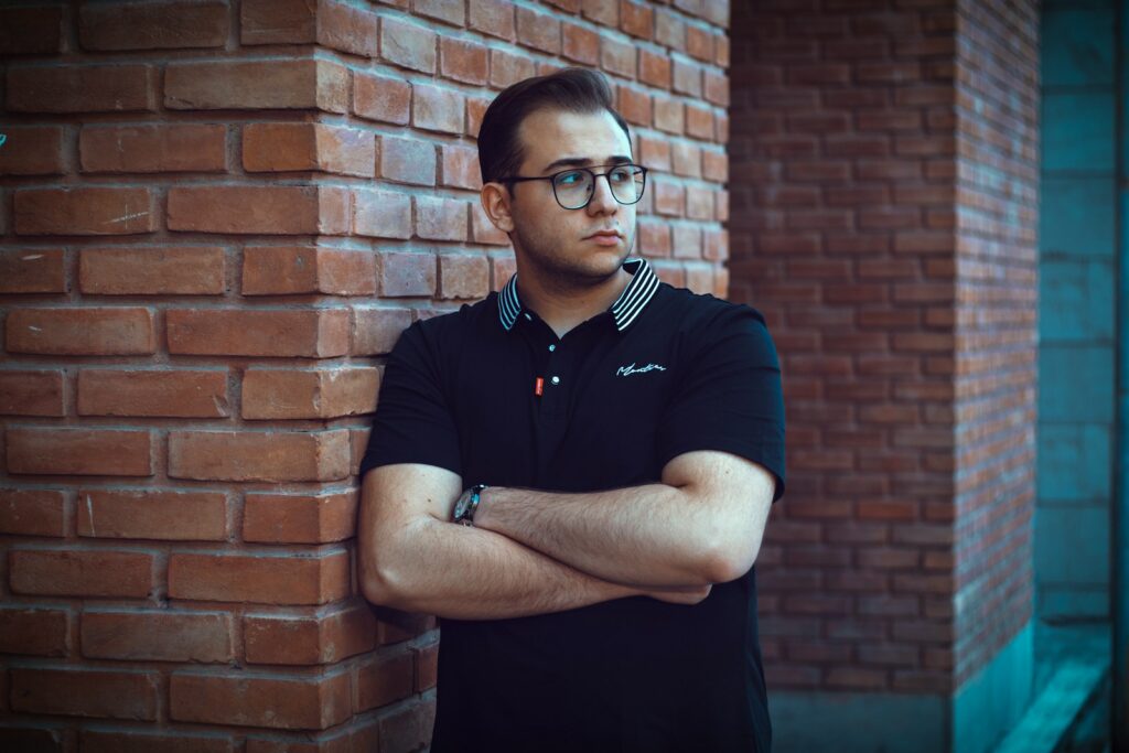 a man leaning against a brick wall with his arms crossed