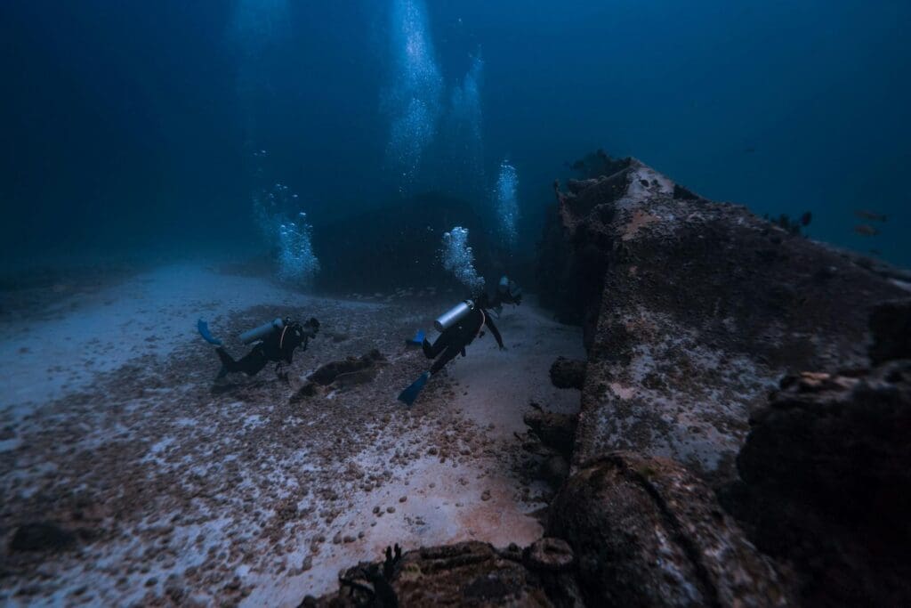 Scuba Divers with Equipment Swimming near Shipwreck Underwater