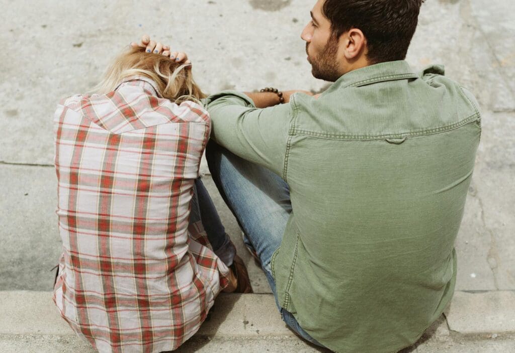 A couple sitting on the street, engaged in a distressed conversation, capturing a moment of emotional tension.