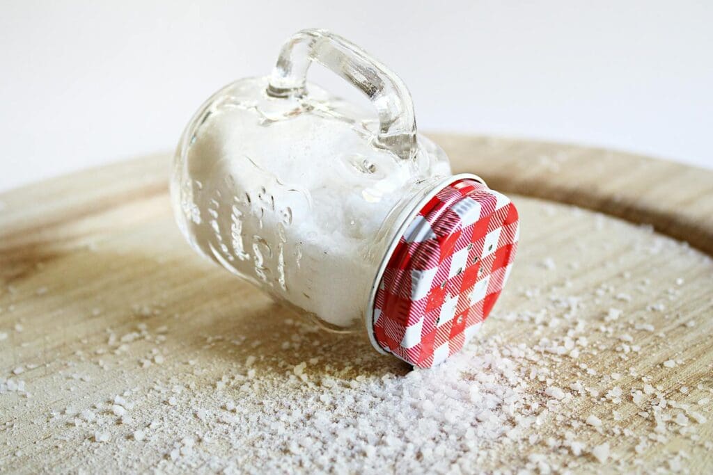 Overturned mason jar with red lid spilling salt on a wooden surface, creating a rustic kitchen scene.