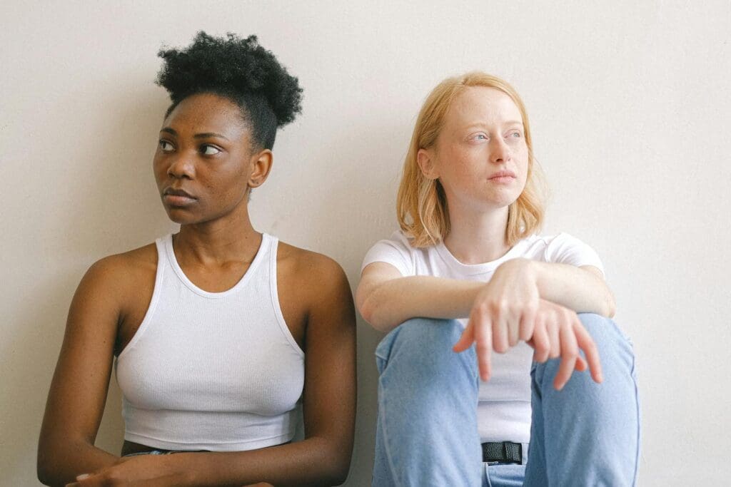 Diverse couple sitting with thoughtful expressions against a plain wall.