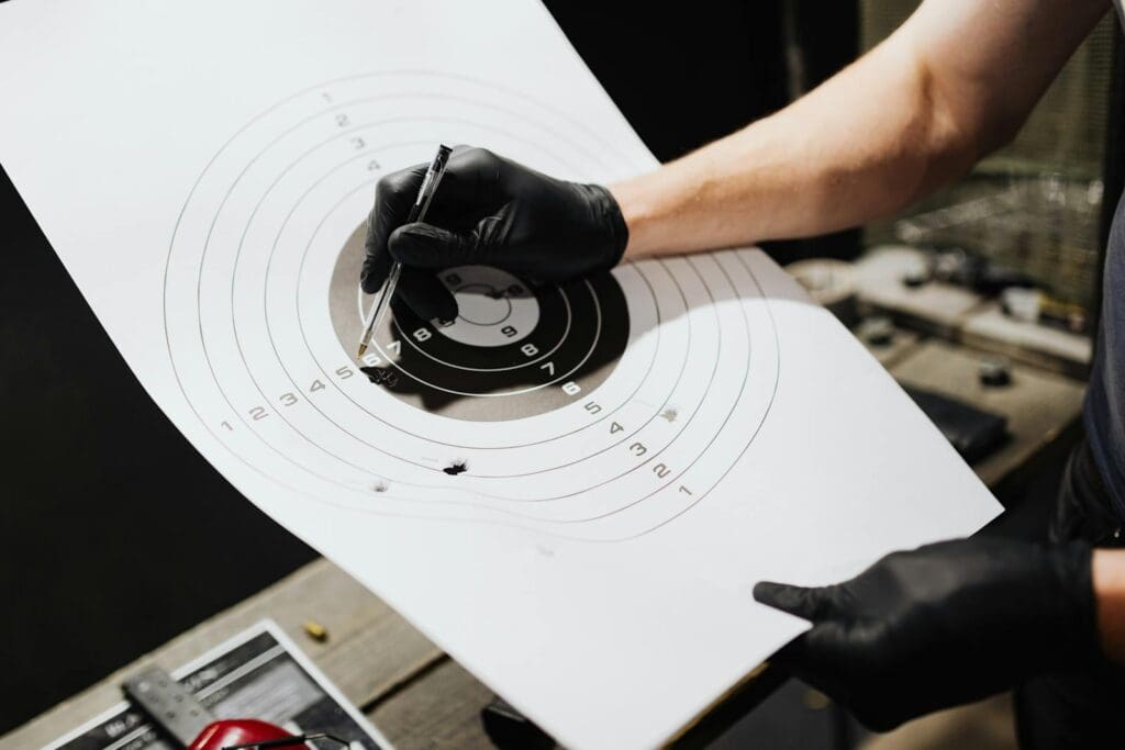 A close-up image of a hand wearing gloves marking a shooting target in a firing range.