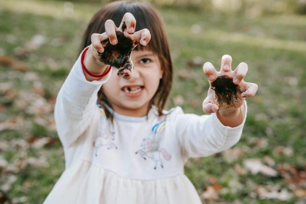 Funny girl with painted hands making scary face while playing in park during Halloween celebration