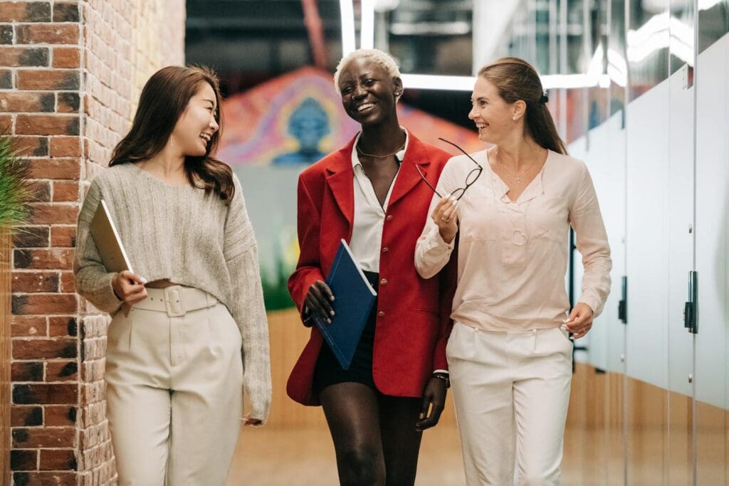 Group of young glad businesswomen in trendy elegant outfits smiling and discussing business strategy in contemporary workspace