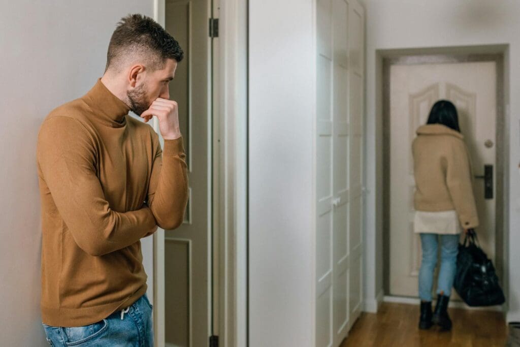 A couple experiencing a tense moment as a woman walks out of the apartment.