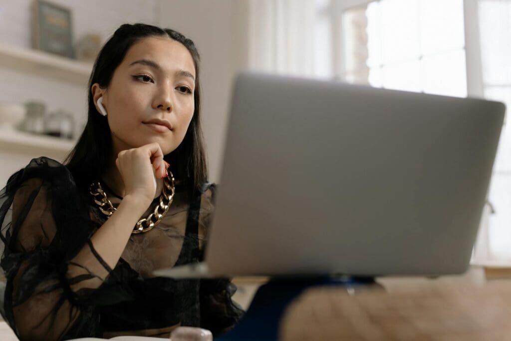 Young woman with wireless earphones working on a laptop indoors, displaying concentration and style.