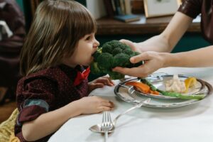 Cute child eating broccoli, promoting healthy eating habits indoors.