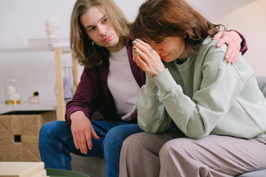 Crop male soothing disappointed crying female in sweatshirt and gray trousers on blurred background