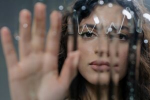 Artistic portrait of a woman touching a wet glass panel, evoking a sense of synesthesia.