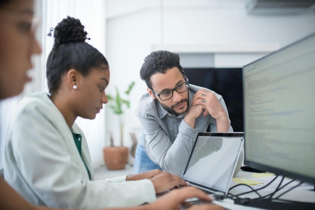 Two people collaborate in a modern office setting, focused on computer work