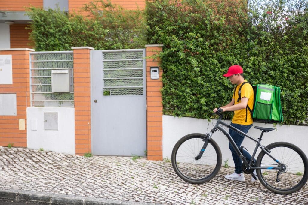 A bicycle courier in casual attire delivers a package at a residential area.