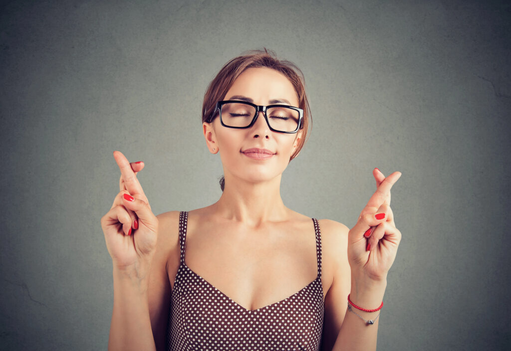 Cute young woman in glasses crosses fingers, making a wish