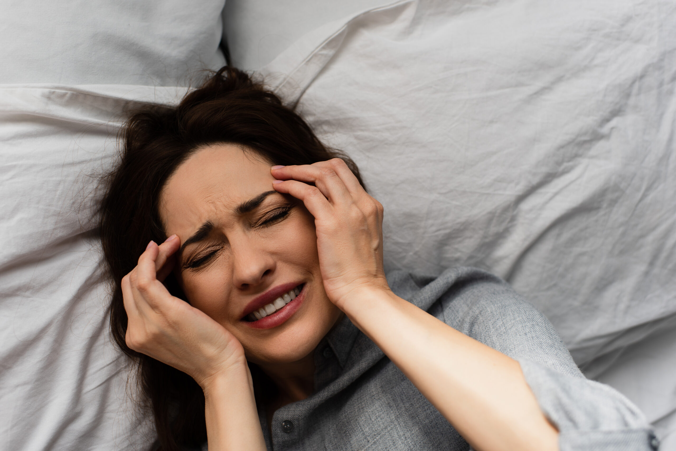 top view of brunette woman suffering from pain and touching head while lying on bed