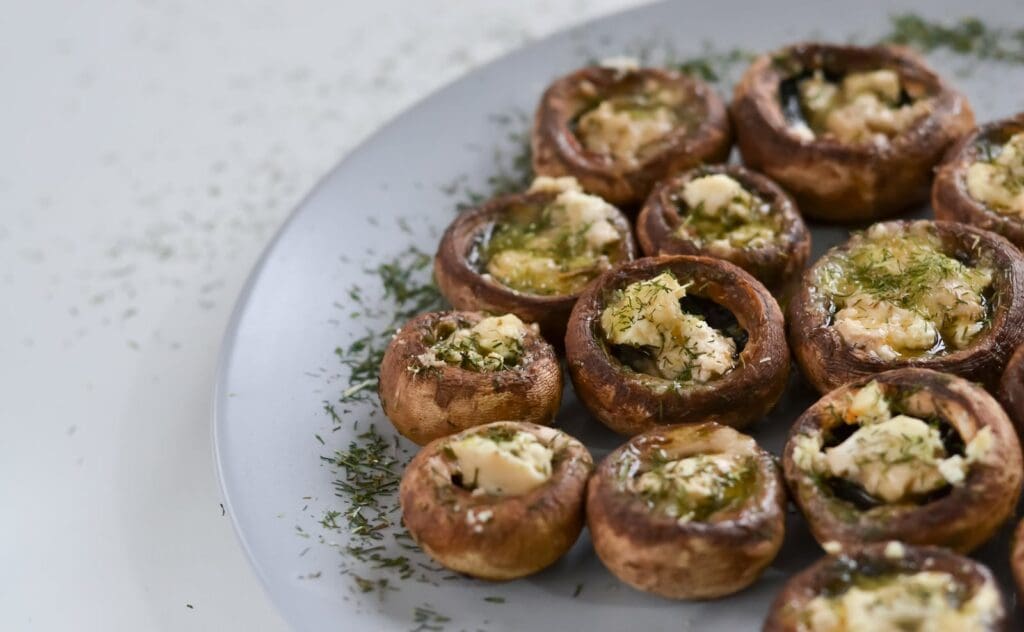 Delicious cream cheese stuffed mushrooms garnished with herbs on a plate.