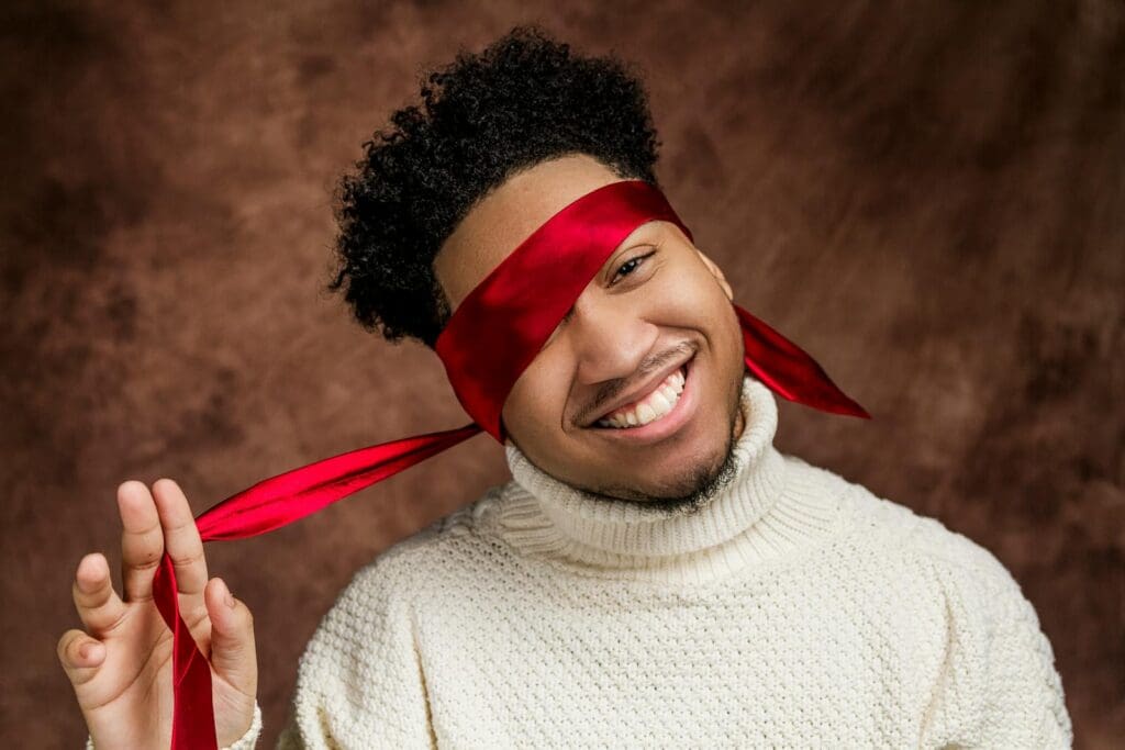 Cheerful young man in a white sweater with a red blindfold, expressing happiness.