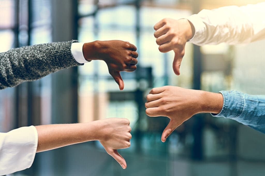 Business people, thumbs down and vote with sign for negative review, feedback or disapproval at office. Closeup of group, employees or team with hand, emoji or disagree for bad news at workplace.