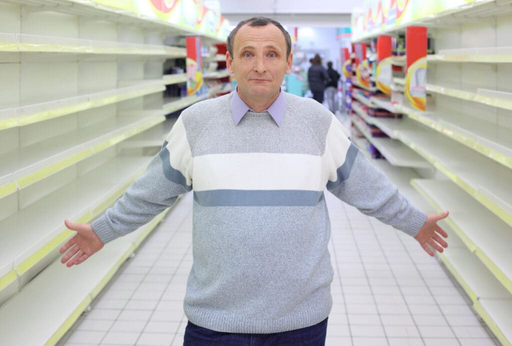 Elderly man stands between empty shelves in shop with dissolved