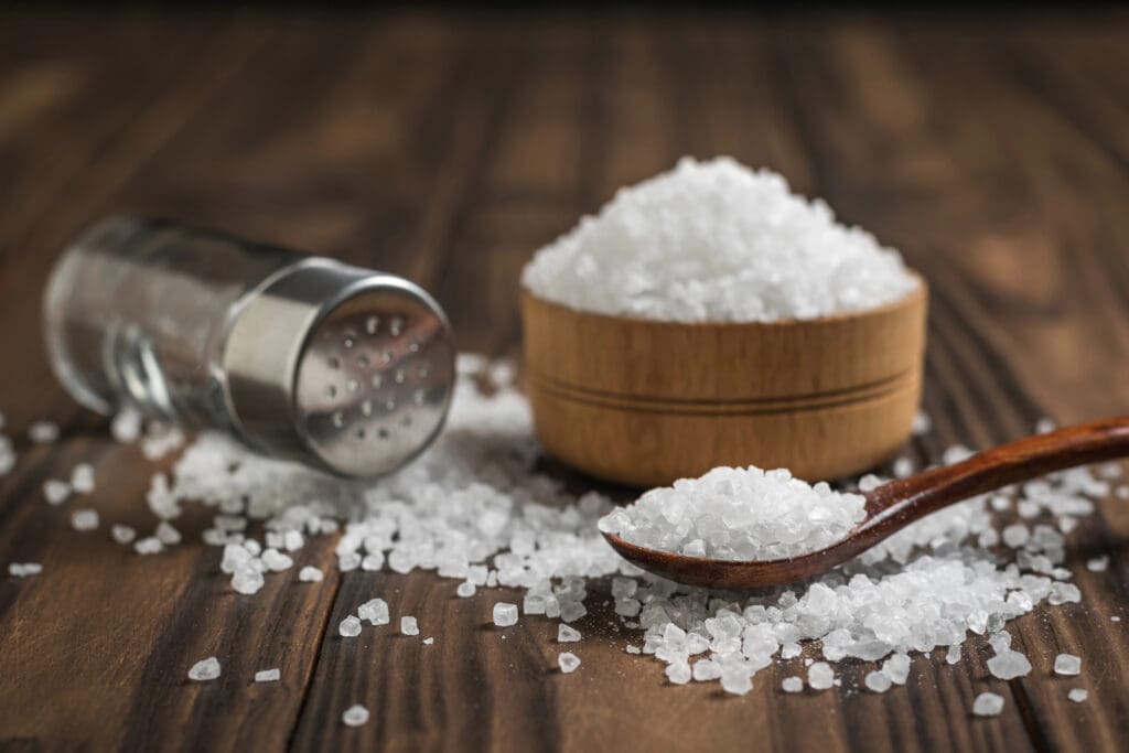 Glass salt shaker, wooden Cup and spoon on the table.