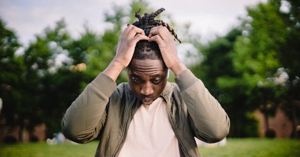 Upset young African American male freelancer clutching head with hands after failure in project while working remotely in park