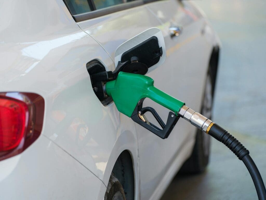 Close-up of a green nozzle refueling a white car at a gas station.