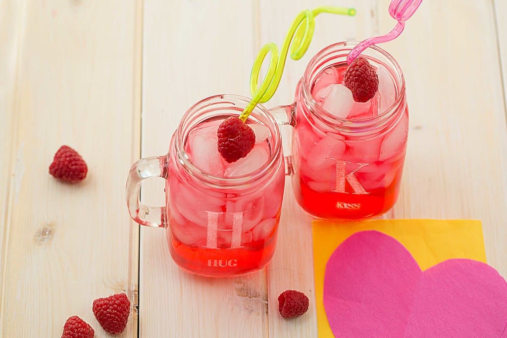 pink lemonade in personalized mason jar glass mugs and raspberries on a table with heart napkin