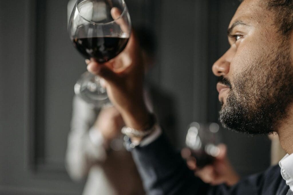 Close-up of a man admiring a glass of red wine indoors, showcasing a moment of elegance.