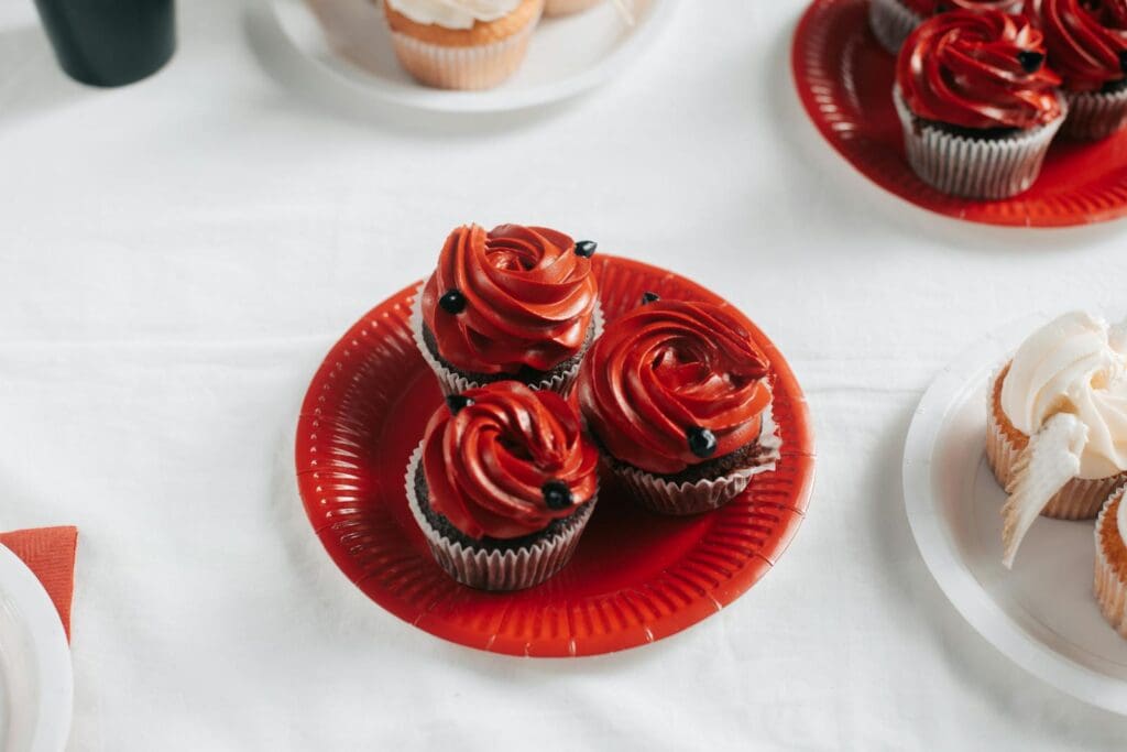 Decorative red velvet cupcakes with frosting on red paper plates, perfect for celebrations.