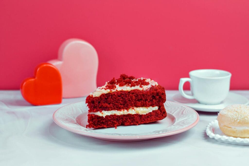 A vibrant still life featuring red velvet cake and a doughnut on a table with heart decorations.