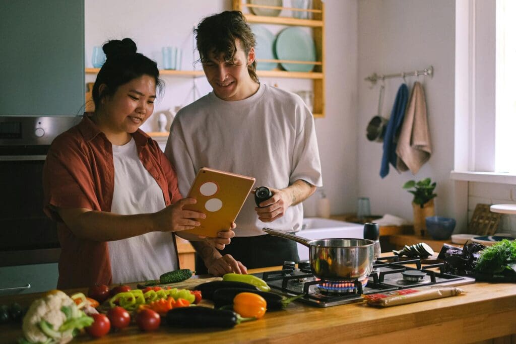 A couple preparing a meal together using a tablet in a modern kitchen setting.